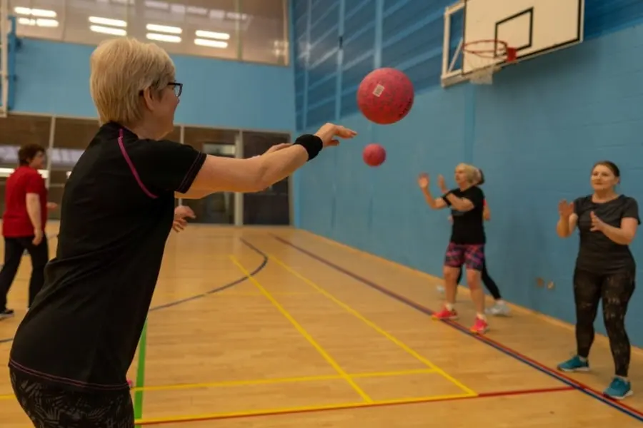 Walking Netball session. Women in the middle of a netball training drill passing pink netball to each other.
