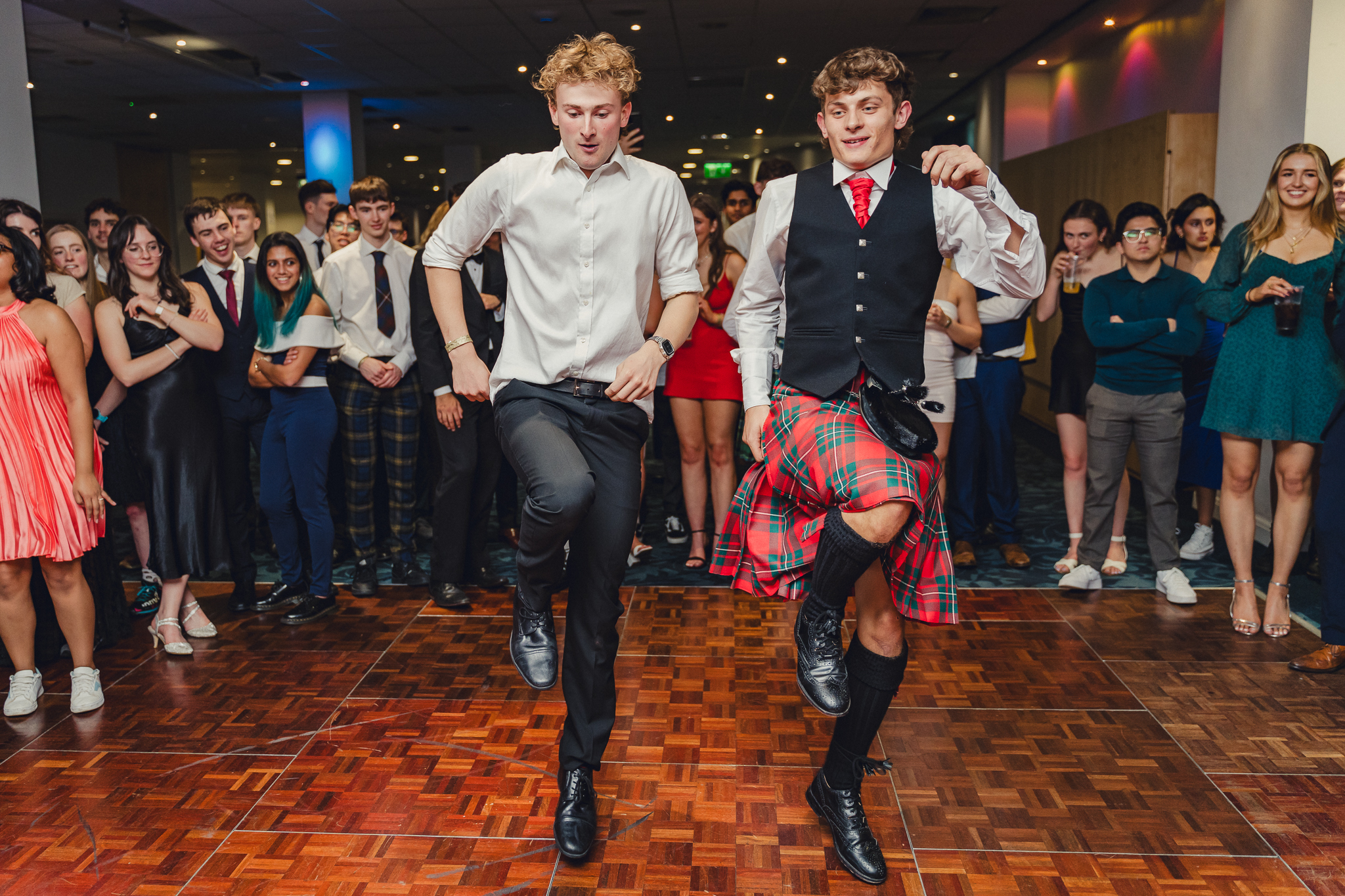 Two male students in middle of dance floor doing synchronised dance. 