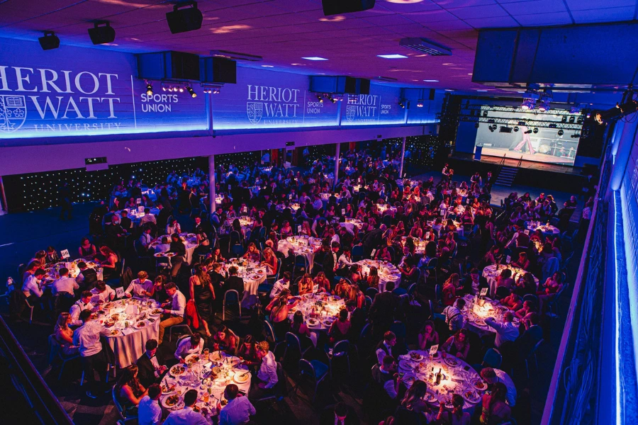 Overhead view of Heriot-Watt Sports Union Ball. Large conference room filled with circular dining tables with students dressed in formal evening wear. 